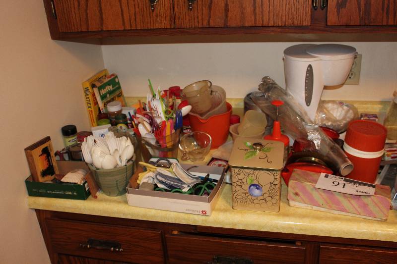 lot 91 image: Counter Top Lot includes measuring cups, plastic silverware, bread pans, frying pans and more