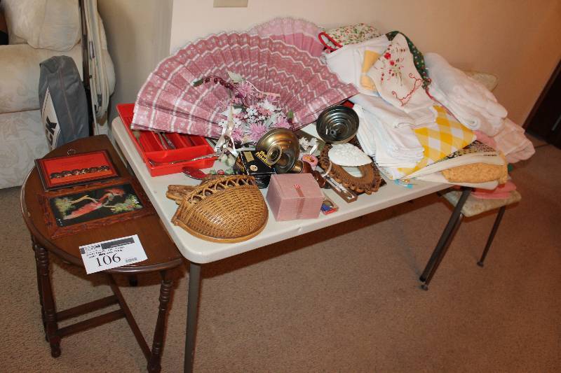 lot 106 image: Table Lot includes end table, fancy rose colored fans (2), silvreware holder, dishcloths and more.  Does not including white folding table