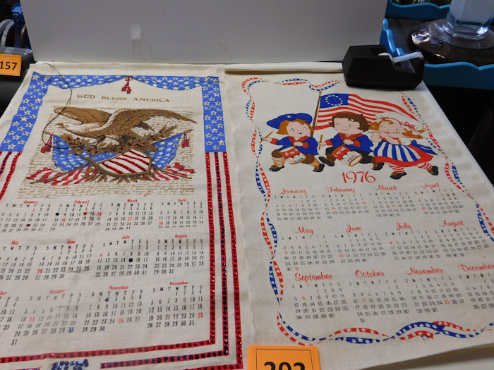 lot 202 image: two wall hanging bicentennial calendars on material